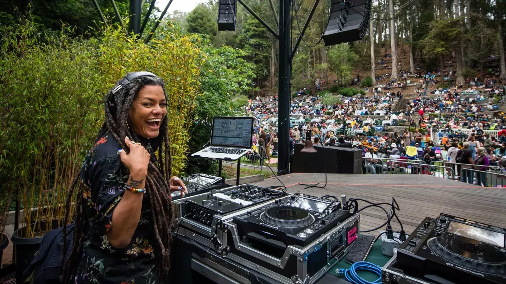 斯特恩格罗夫节(Stern Grove Festival)에서 DJ를 하고 있는 한 여성이 어깨 너머로 카메라를 바라보며 미소를 짓고 있습니다.